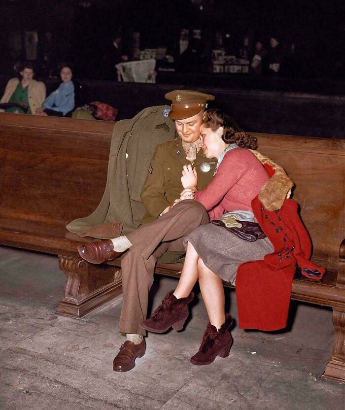 Couple sitting on a wooden bench in historical attire, representing a vastly different world from today in this vintage photo.