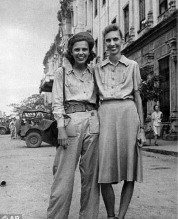 Two women smiling on a street wearing 1940s clothing in a historical photo representing a vastly different world.
