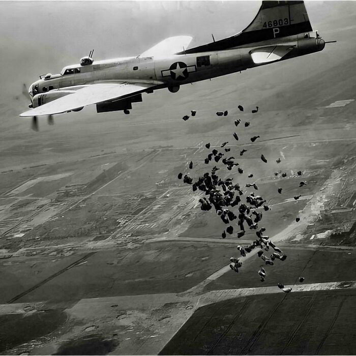 Black and white historical photo of a military plane dropping supplies over a vast landscape, representing a different world.