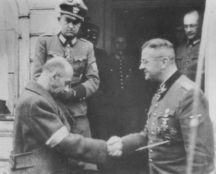 Historical black and white photo showing a handshake between a prisoner and a uniformed officer during World War II.