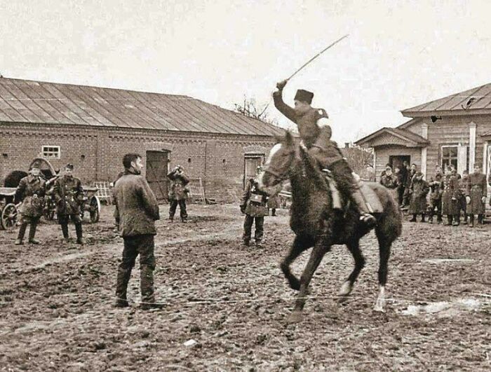 Historical photo showing a soldier on horseback wielding a whip in a muddy courtyard surrounded by onlookers.
