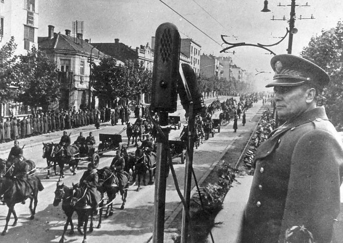 Black and white historical photo of a military parade with soldiers on horseback and an officer observing the event.