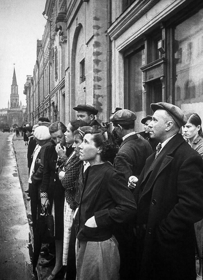 Black and white historical photo of people standing in a line on a city street, representing a vastly different world.