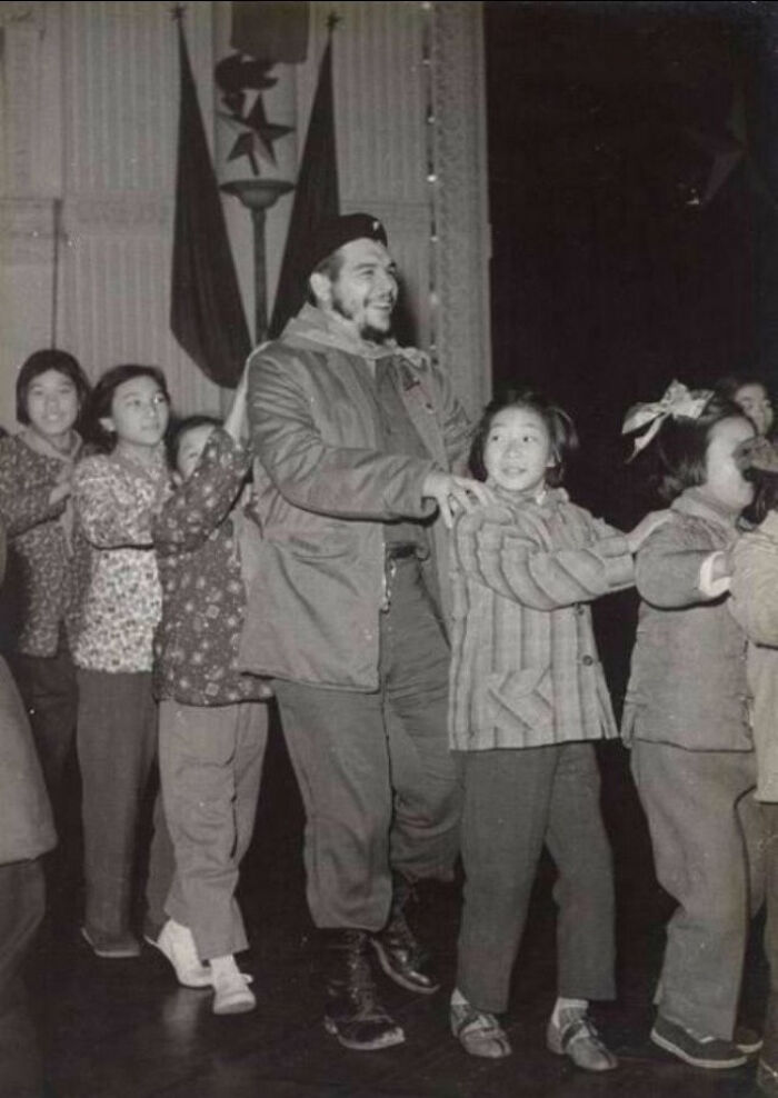 Black and white historical photo of a man and children holding hands in a playful line, representing a vastly different world.