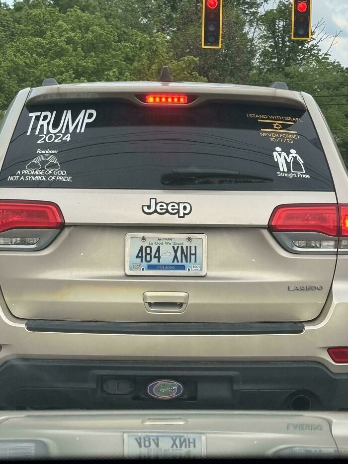 Rear view of a Jeep with unhinged bumper stickers including political and pride messages at a red traffic light.