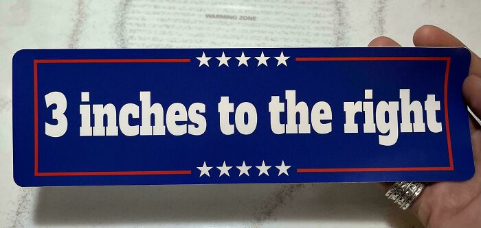 Hand holding a blue bumper sticker with white text that reads 3 inches to the right, a hilarious unhinged bumper sticker.