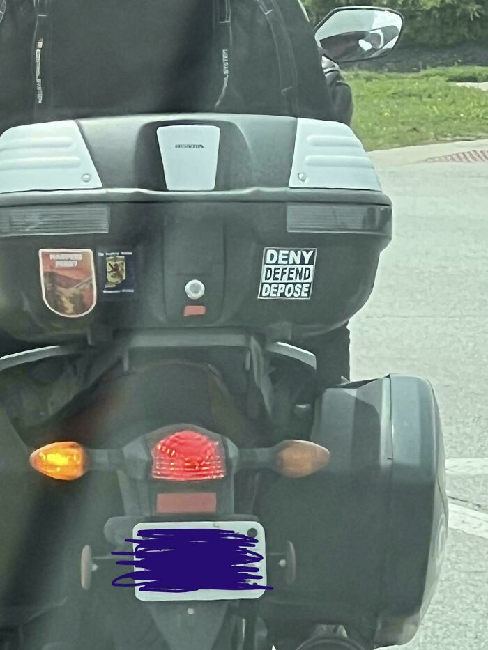 Motorcycle with humorous and unhinged bumper stickers including deny, defend, depose text on the back storage box.