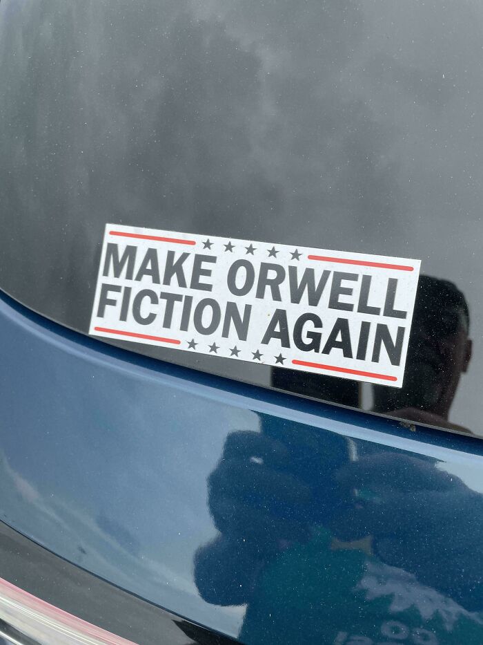Bumper sticker on blue car reading make Orwell fiction again with stars and red lines, a hilarious and unhinged bumper sticker.