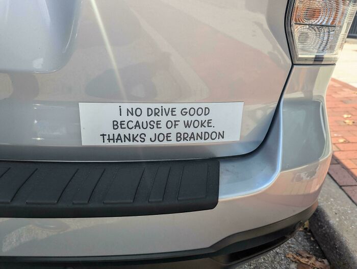 Bumper sticker on a silver car reading humorous and unhinged message about driving and politics.