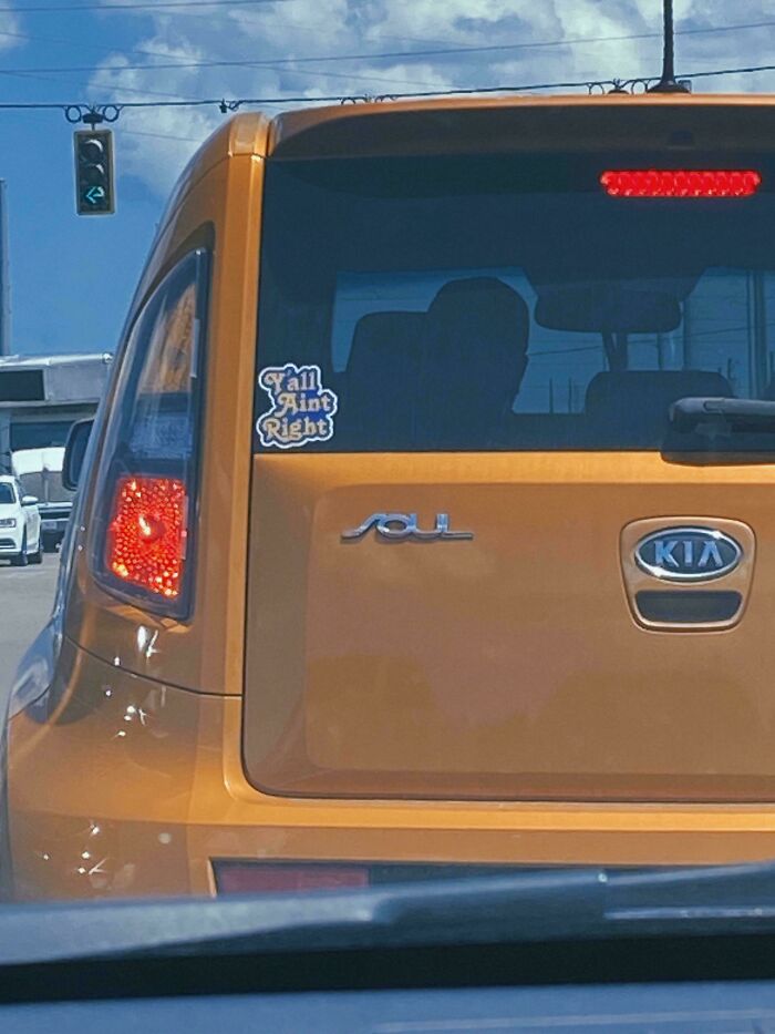 Orange Kia Soul car with a hilarious and unhinged bumper sticker reading Y'all Ain't Right on the rear window.