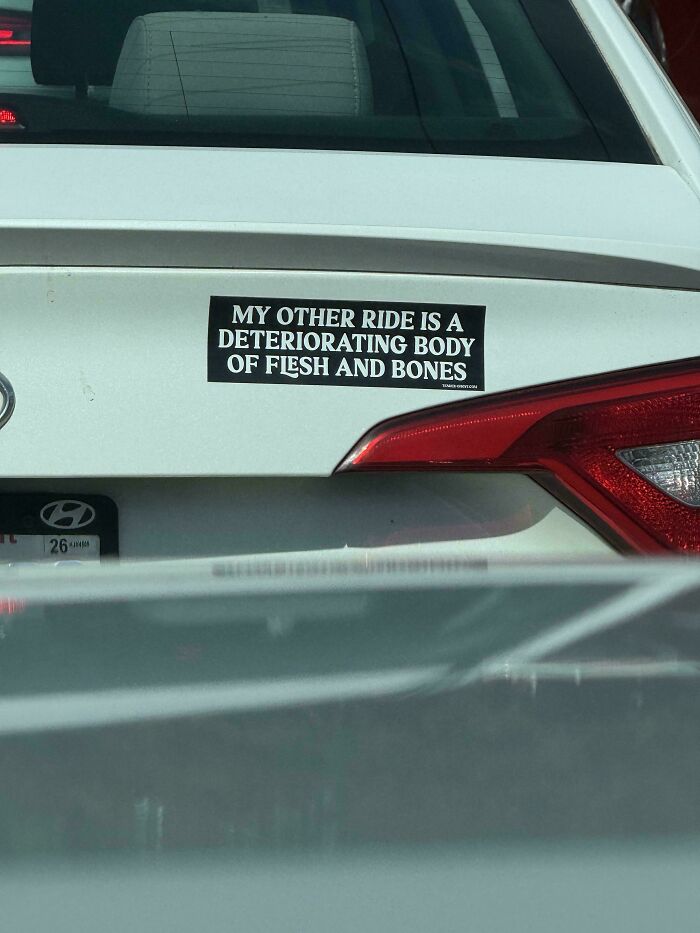 White car with a hilarious bumper sticker that reads a joke about a deteriorating body of flesh and bones.