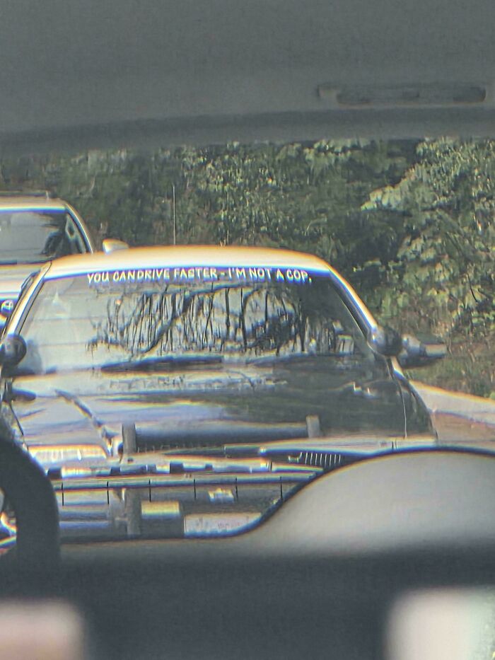Car with a humorous windshield bumper sticker saying you can drive faster, I'm not a cop, spotted in traffic.