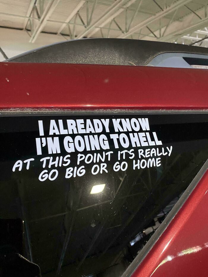 Hilarious and unhinged bumper sticker on a red car window reading go big or go home message.