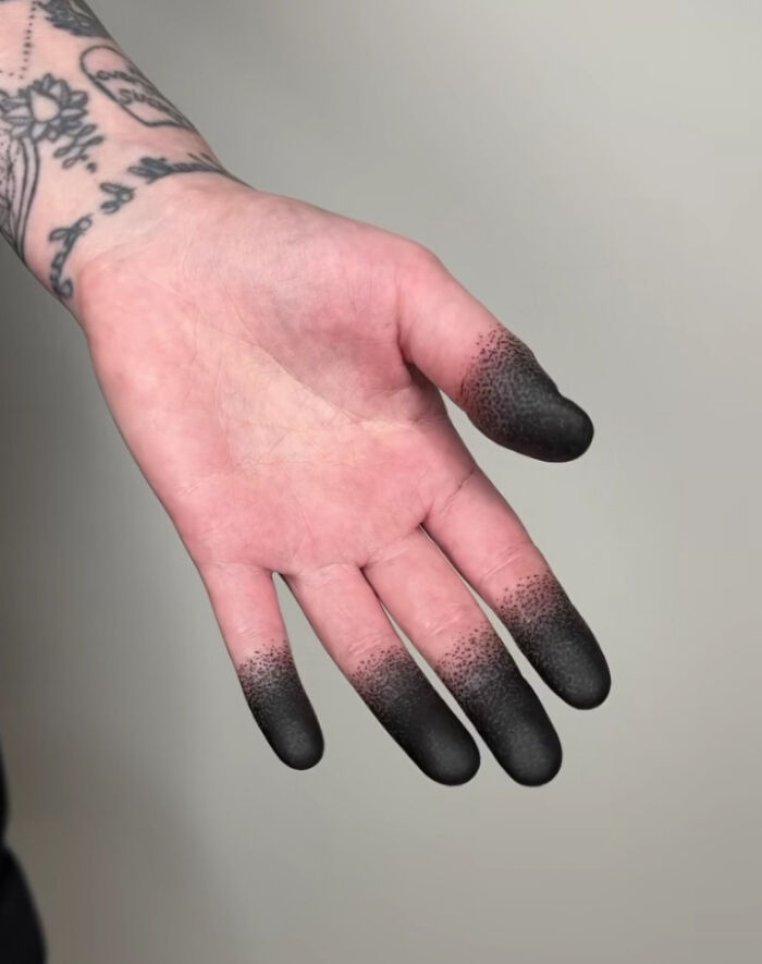 Hand with tattooed black fingertips fading into natural skin, an example of truly awful tattoos that are permanent and unusual.