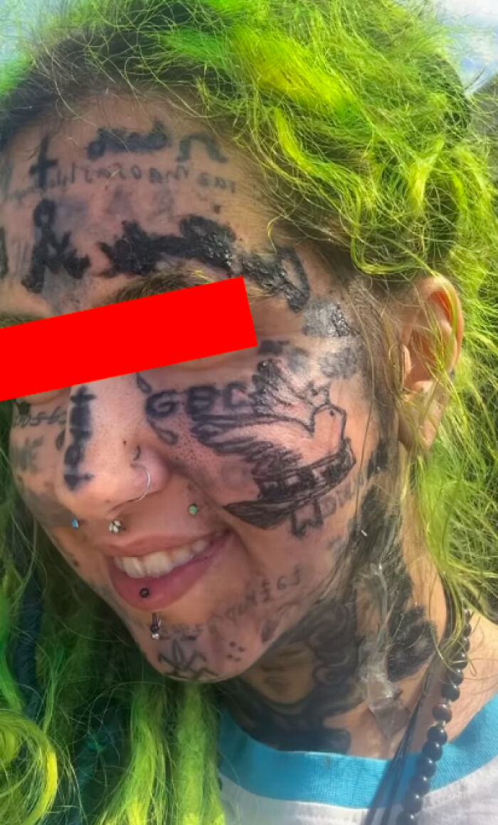 Person with numerous face tattoos including a bird and text, showcasing truly awful tattoos with bright green hair and facial piercings.