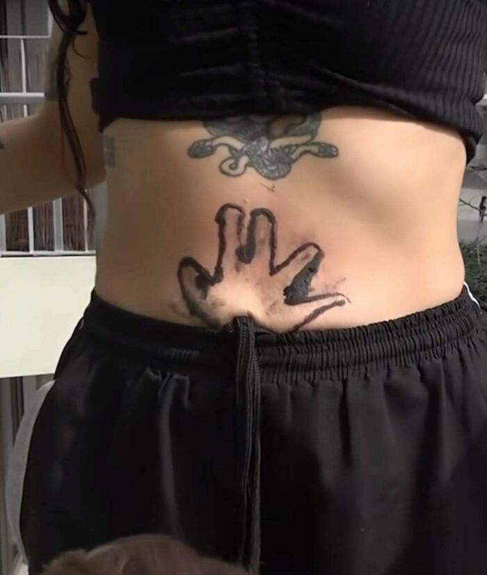 Tattoo of a distorted hand with smudged black ink on a lower abdomen, one of the truly awful tattoos that are funny and tragic.