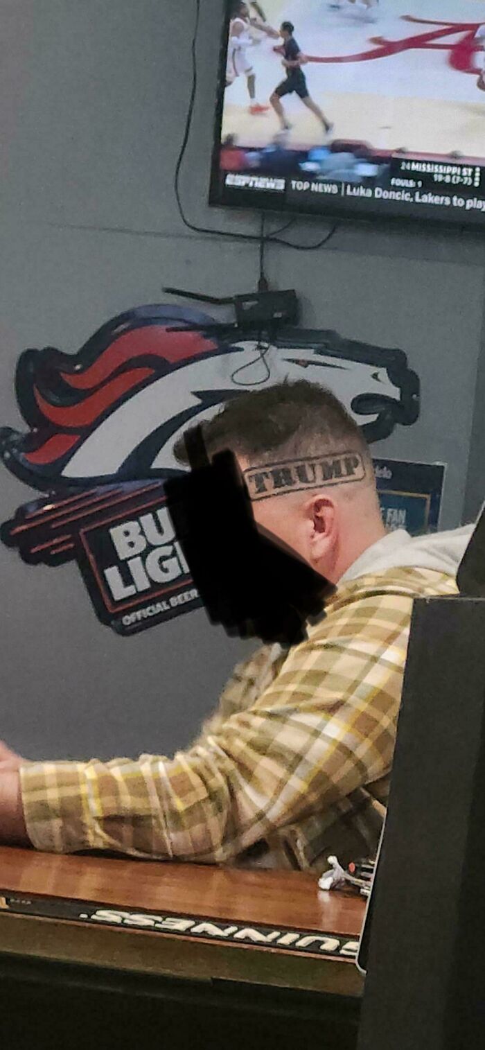Man with a "TRUMP" head tattoo sitting at a bar with sports and beer logos, an example of truly awful tattoos.