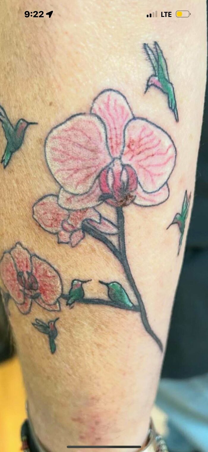 Tattoo of a pink flower with multiple green hummingbirds on a person's forearm, showing a truly awful tattoo design.