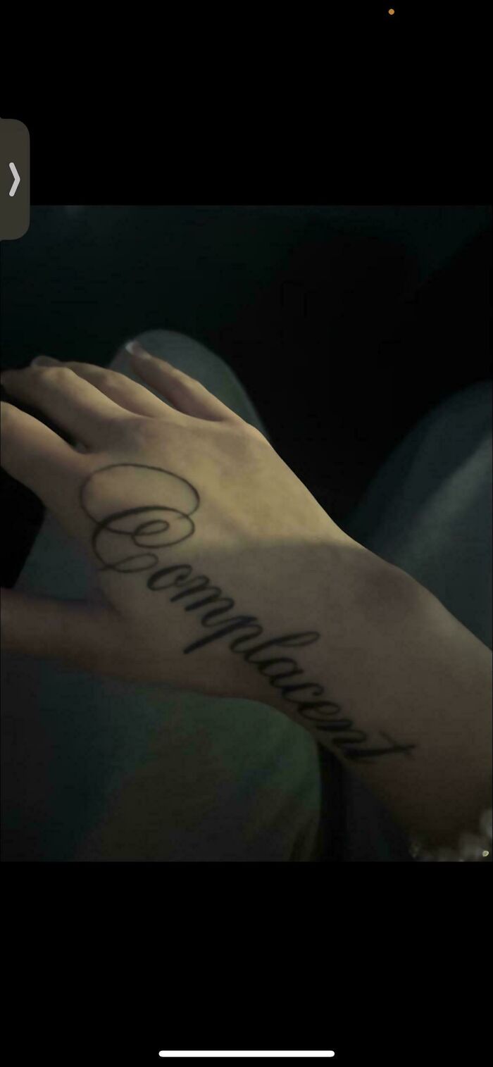 Hand tattoo with the word complacent in cursive, an example of truly awful tattoos that are funny and tragic.