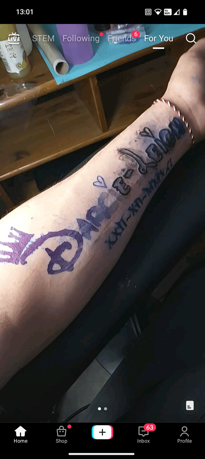 Arm with a truly awful tattoo drawn in marker featuring a crown, hearts, and illegible text in black and purple ink.