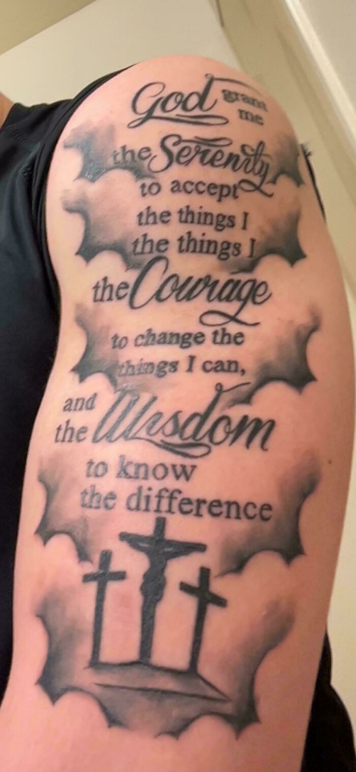 Tattoo of a misspelled inspirational quote surrounded by shading and three crosses on upper arm, a truly awful tattoo example.