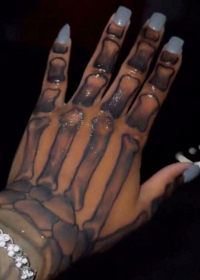 Hand with a detailed skeleton tattoo covering the back, featuring long nails and a bracelet, showcasing truly awful tattoos.