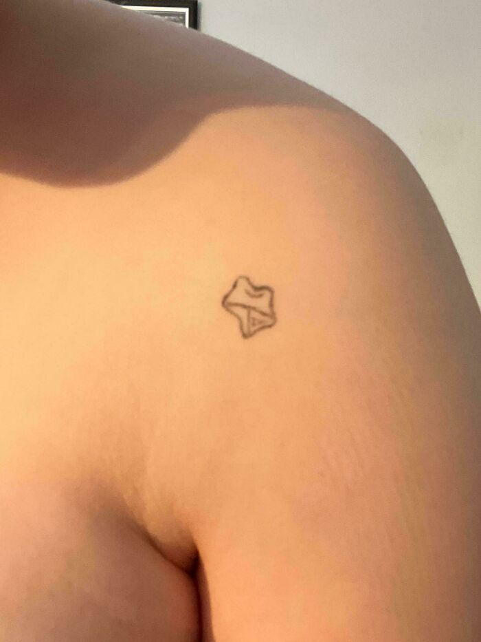 Small poorly drawn outline tattoo on a shoulder, one of the truly awful tattoos that are funny and tragic.