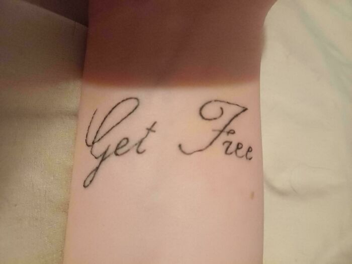 Close-up of a truly awful tattoo on wrist with handwritten style text that reads Get Free, showcasing funny and tragic ink.