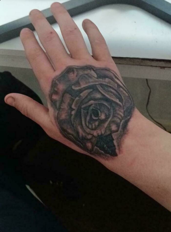 Close-up of a hand with a poorly executed rose tattoo, one of the truly awful tattoos that are funny and tragic.