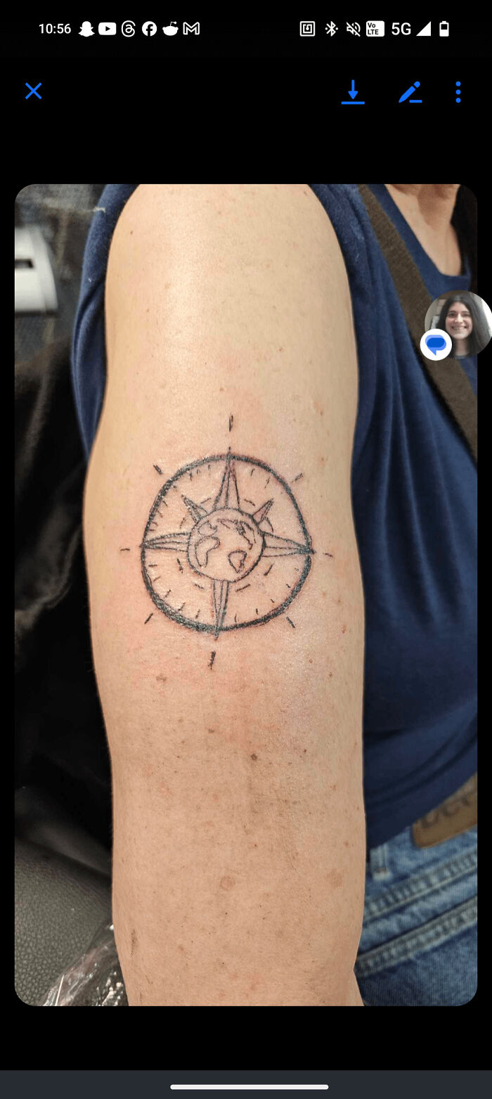 Arm tattoo of a poorly drawn compass with a globe in the center, showcasing truly awful tattoos.