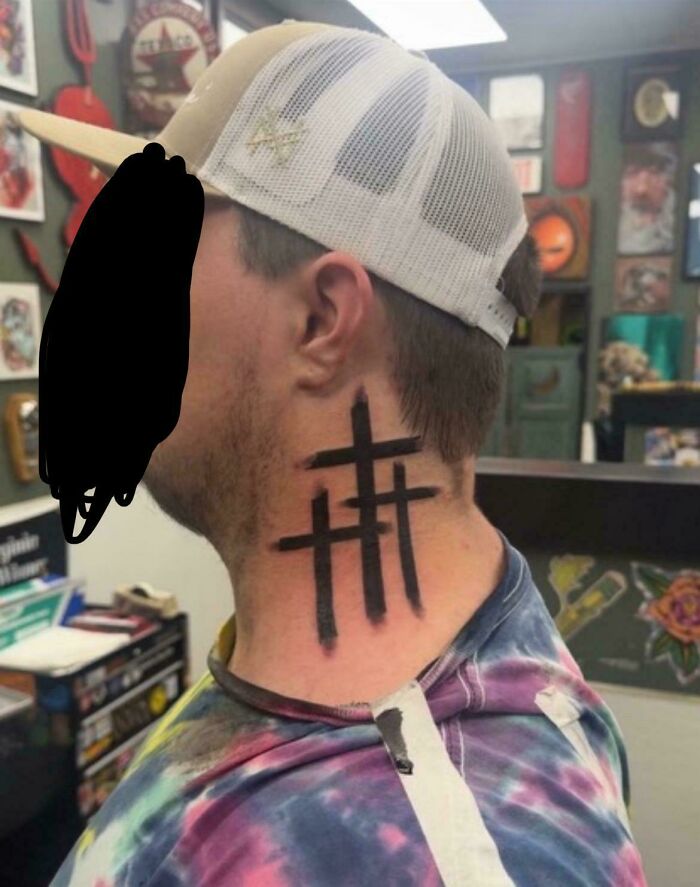 Man with a neck tattoo of three black crosses in a tattoo parlor, showcasing truly awful tattoos that are funny and tragic.