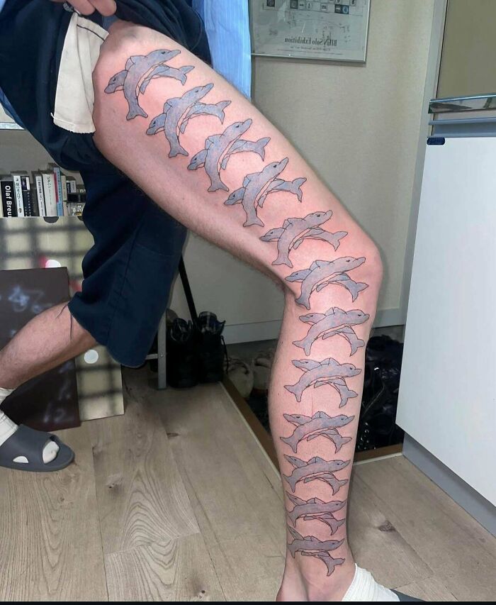 Leg tattoo featuring a repeated pattern of dolphins in a unique design, showcasing truly awful tattoos with a funny twist.