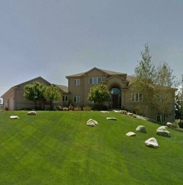 Exterior view of a large home, inspired by mansions, featuring a sloped lawn with rocks, resembling a Temu version.