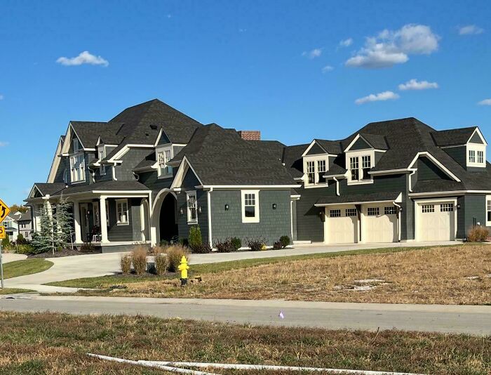 A newly built mansion-inspired home, resembling a Temu version, with multiple gables and a large driveway.