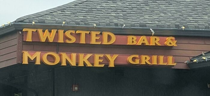A bar and grill sign with poor design reads 'Twisted Bar & Monkey Grill', creating a hilariously confusing message.