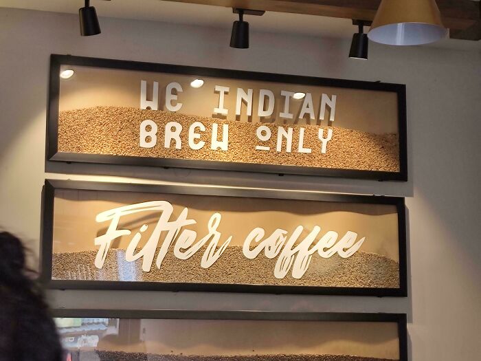 Cafe signs with poor design show 'We Indian Brew Only' and 'Filter Coffee' over coffee beans, humorously confusing.