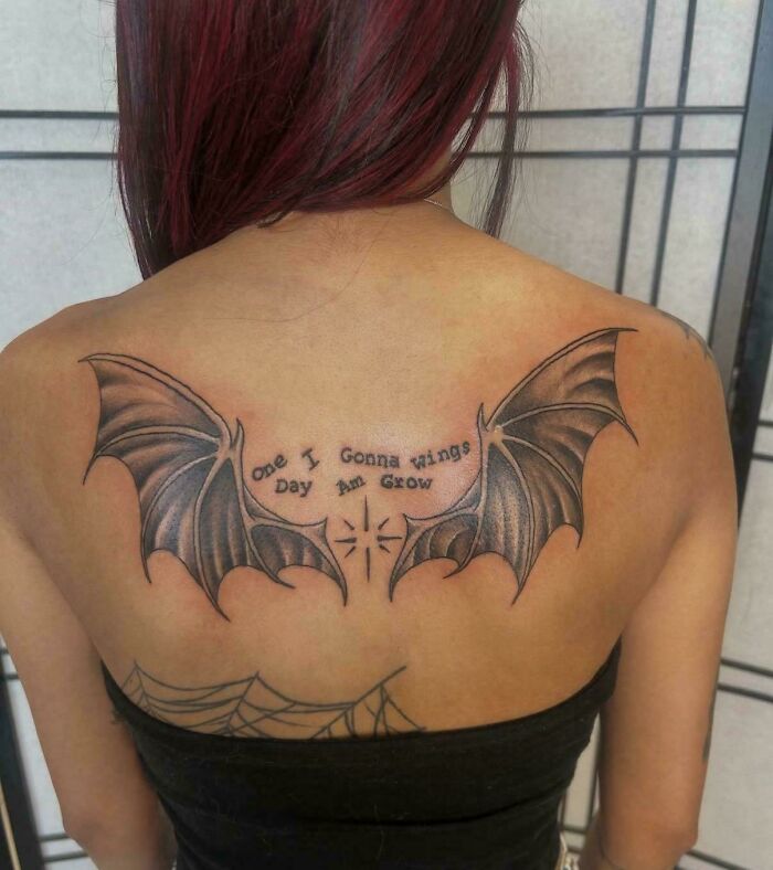 A woman's back with a tattoo of bat wings and a confusing message that says ONE I GONNA WINGS DAY AM GROW, showing poor sign design.