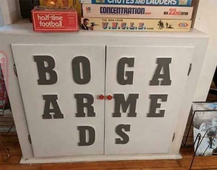 A hilariously confusing sign design on a cabinet that spells out BOGARDS and BOARDS, with board games stacked on top.