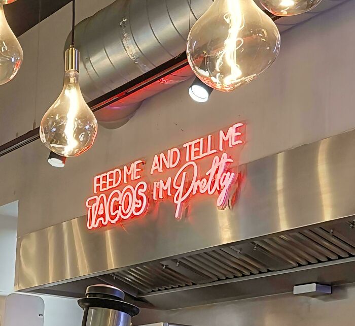 A neon sign with poor sign design that reads Feed Me Tacos and Tell Me Im Pretty, leading to a confusing message.
