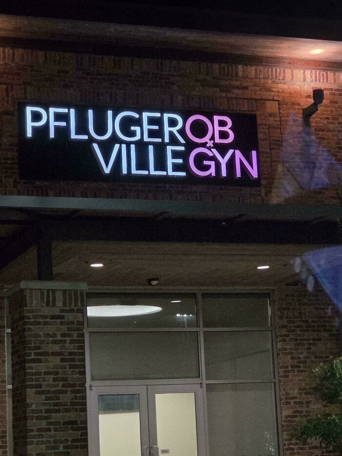 A building at night with a confusing sign design that reads Pfluger OB Ville Gyn in neon pink and white letters.