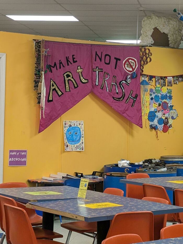 A sign design in an art room that reads Make Art Not Trash, with colorful artwork and tables in the background.