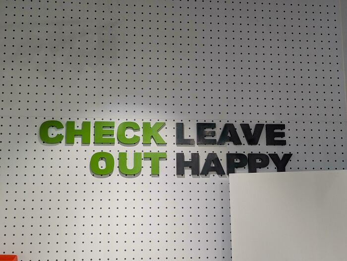 A hilariously confusing sign design that reads Check Leave Out Happy in green and black letters on a white polka dot wall.