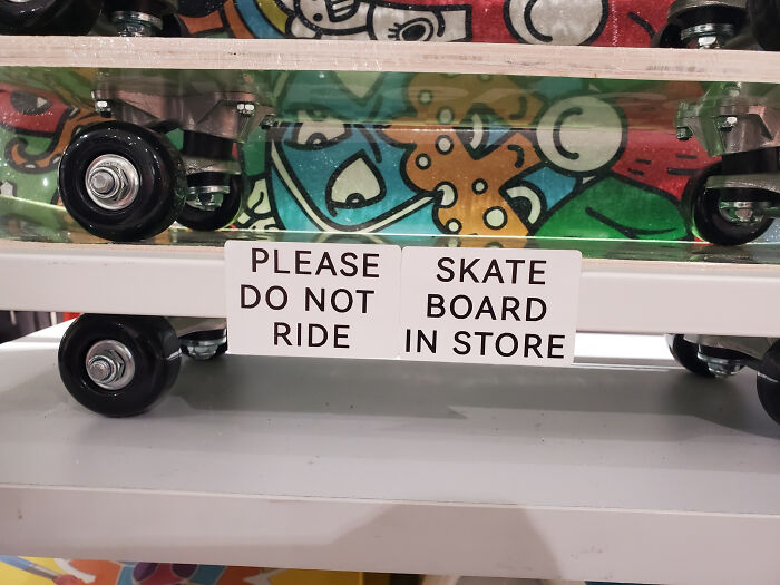 A retail shelf displaying multiple skateboards with a confusing sign design that reads: PLEASE DO NOT RIDE SKATE BOARD IN STORE.