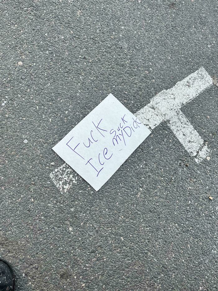 A small white sign with hand-written confusing message lying on asphalt next to a white painted line, showing poor sign design.