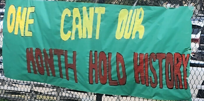 A green banner with yellow and red text, displaying confusing sign design that reads: ONE CANT OUR MONTH HOLD HISTORY.