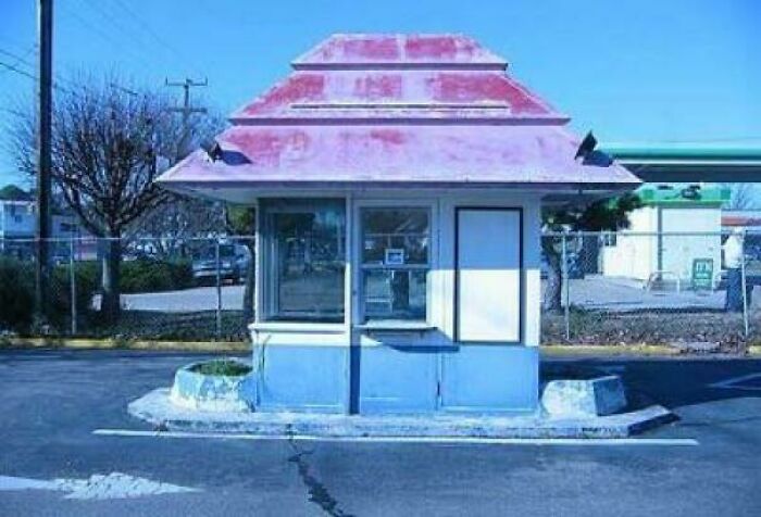 Small abandoned vintage drive-thru booth with faded red and blue paint, evoking nostalgic pics and classic roadside memories.