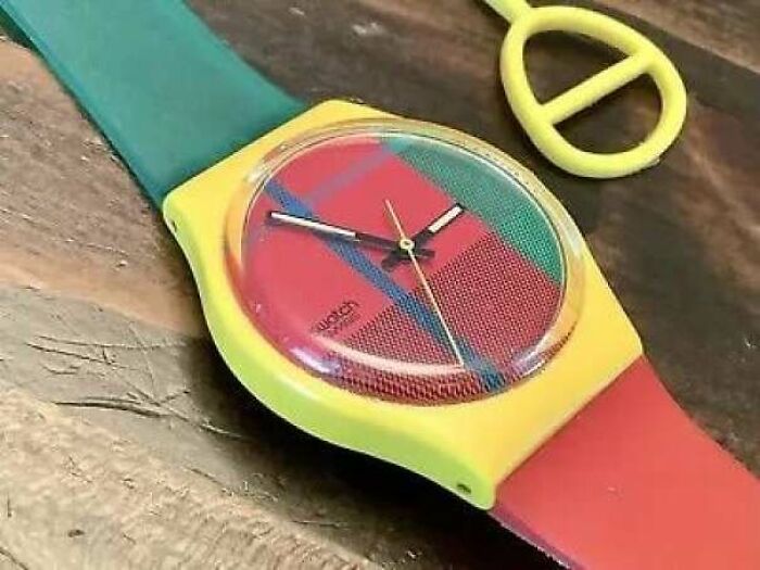 Colorful vintage Swatch watch with yellow, red, and green design resting on a wooden surface, evoking nostalgic pics and references.