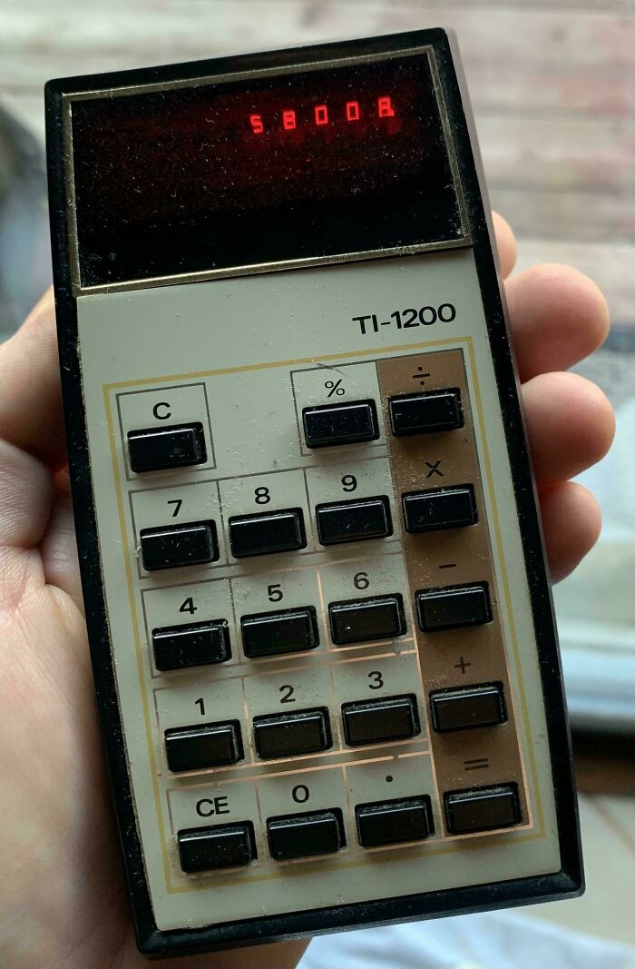 Vintage TI-1200 calculator with red LED display showing numbers, nostalgic gadget from past decades held in hand.