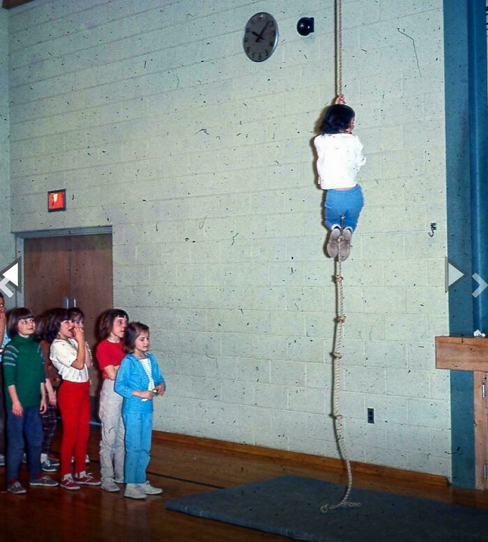 Children in retro gym clothes taking turns climbing a rope in a vintage school gym, evoking nostalgic pics and references.
