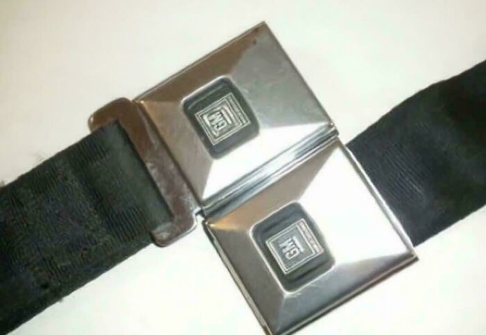 Retro black fabric airplane seatbelt with classic metal buckle featuring vintage GM logo, evoking nostalgic memories.